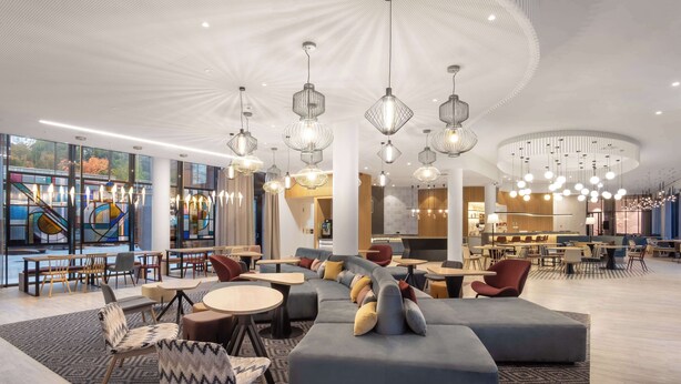 A modern hotel lobby with a curved seating area, multiple dining tables, and contemporary lighting fixtures. - Hampton By Hilton Tallinn (Tallinn)