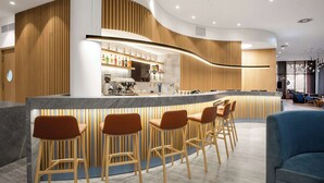 A modern bar area with wooden accents, bar stools, and a counter with various bottles. - Hampton By Hilton Tallinn (Tallinn)