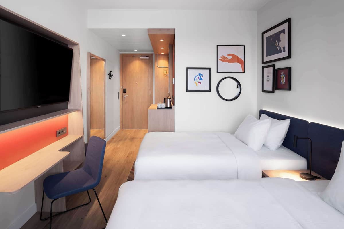 A hotel room with two beds, a desk, a TV, and a chair.