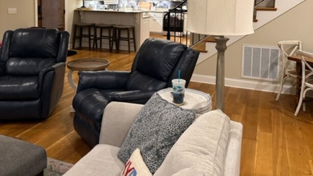 Una sala de estar con sofá, dos sillones, una mesa de centro y una escalera que da a una zona de cocina.