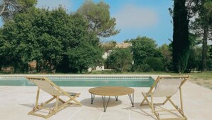 A poolside area with two wooden lounge chairs and a small round table. - Ahouu - Gîte with swimming pool - Pic Saint-Loup (Sauteyrargues)