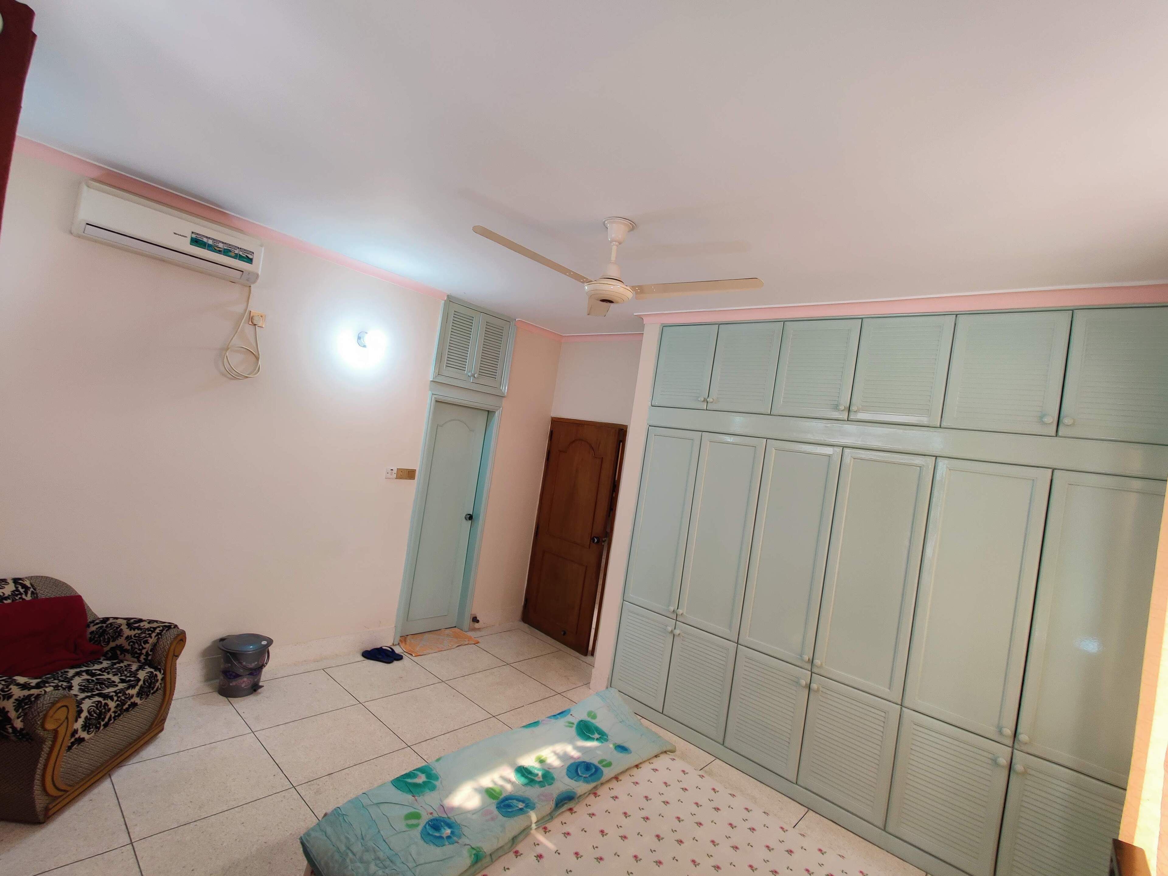 Quarto com cama, guarda-roupa, ventoinha no teto, ar condicionado e uma porta.