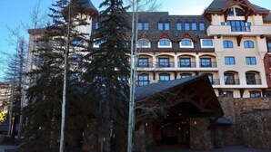 A multi-story hotel with a stone facade, large windows, and a prominent entrance with a wooden structure. - Luxury Hotel Room With 2 Queen Beds in Lionshead Village (Vail)