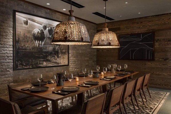 A dining area with a long wooden table set for six, two hanging pendant lights, a large framed picture of cattle, and a geometric wall design. - Luxury Hotel Room With 2 Queen Beds in Lionshead Village (Vail)