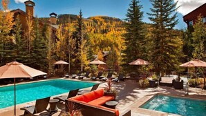 A pool area with lounge chairs and umbrellas, surrounded by trees and a mountain backdrop. - Luxury Hotel Room With 2 Queen Beds in Lionshead Village (Vail)
