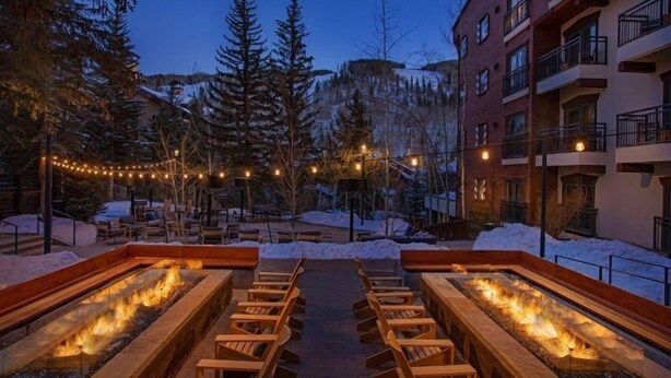 An outdoor seating area with fire pits and wooden benches, surrounded by snow and trees. - Luxury Hotel Room With 2 Queen Beds in Lionshead Village (Vail)