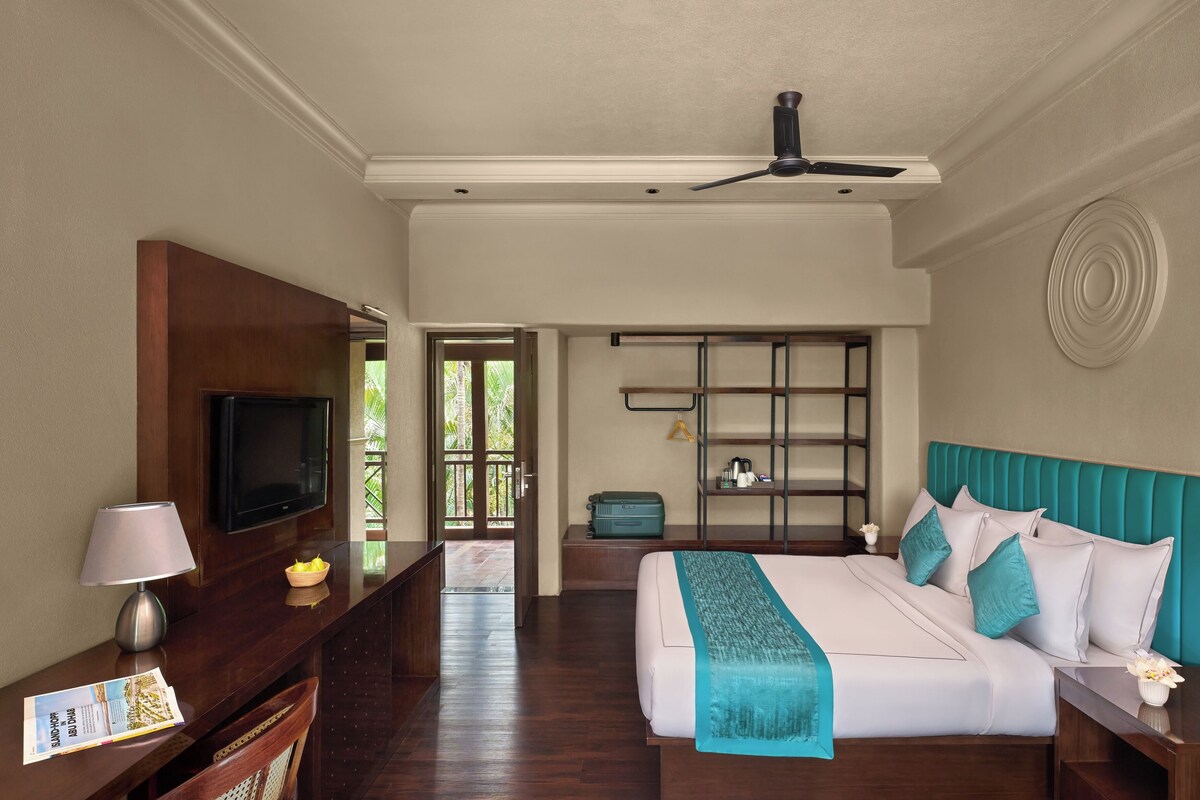 A hotel room with a bed, a TV, a desk with a lamp, and a view of the outdoors.