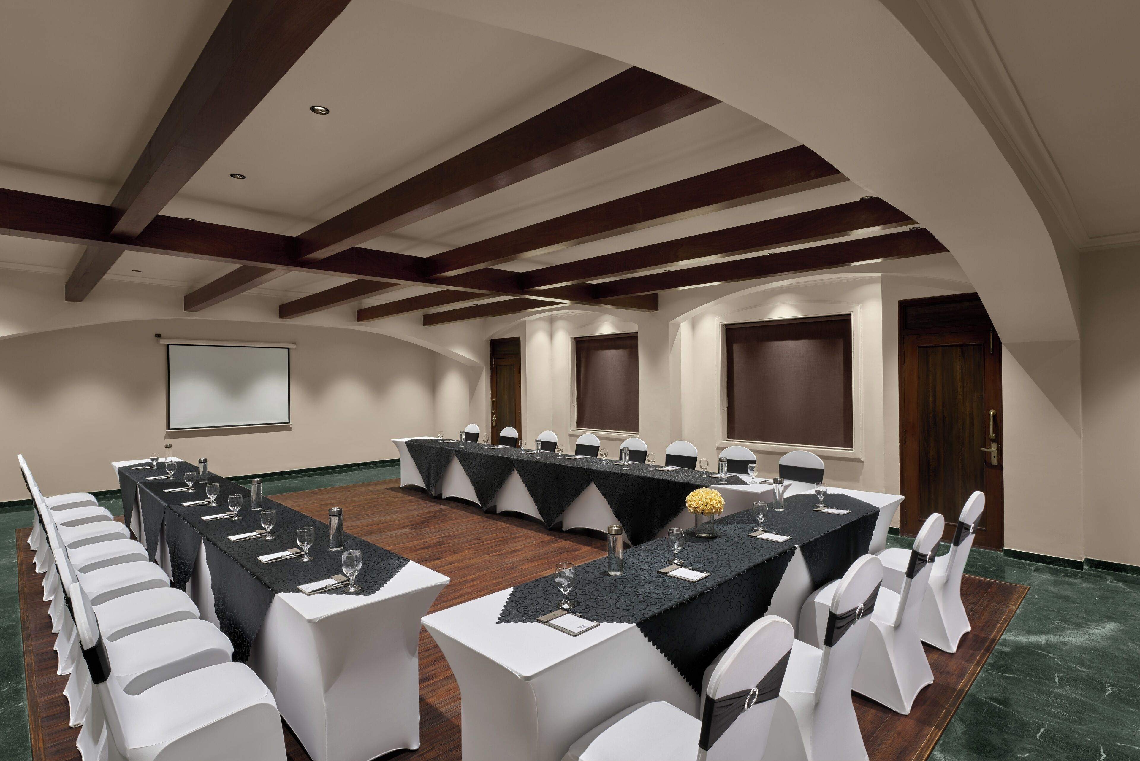 A conference room with a long table, white chairs, and a projector screen.