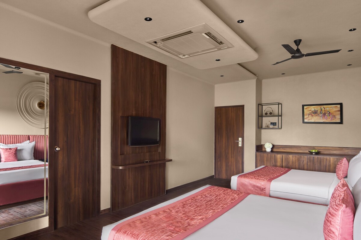A hotel room with two beds, a ceiling fan, a mounted TV, and a wooden wardrobe.