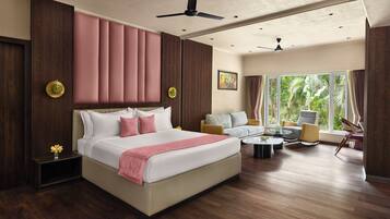 A hotel room with a large bed, a sofa, a coffee table, and a view of greenery through the window.