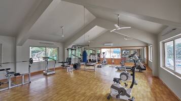Un gimnasio amplio con diverso equipo de ejercicio, ventanas grandes y techos altos.
