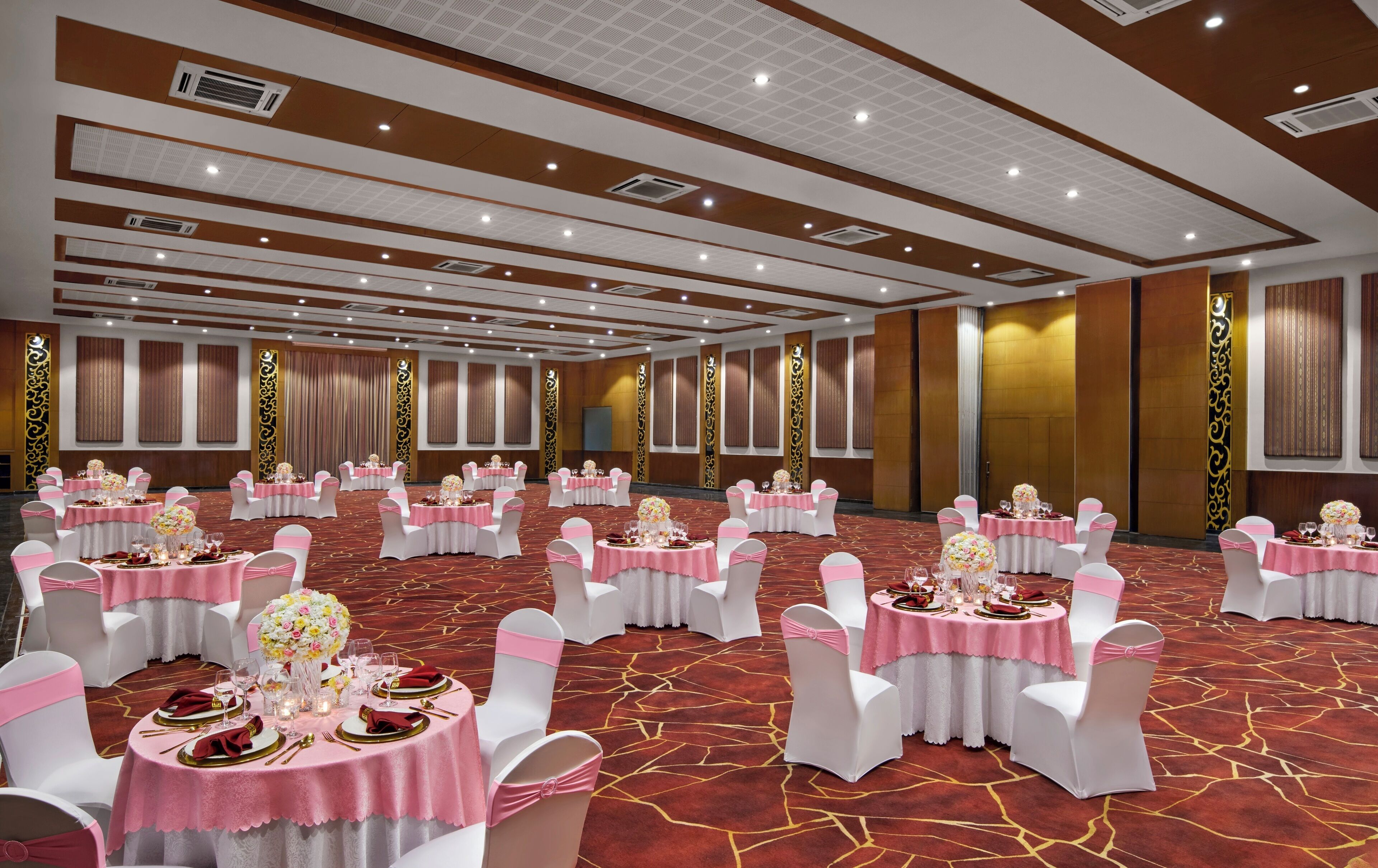 Une salle de banquet avec des tables rondes, des chaises blanches et des touches de rose.