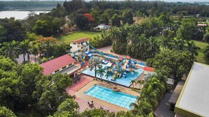 A water park with multiple slides and a swimming pool surrounded by lush greenery and a lake in the background. - DGV Resort by Treat, Silvassa (Silvassa)