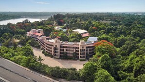 A multi-story building with a curved roof, surrounded by lush greenery and a river in the background. - DGV Resort by Treat, Silvassa (Silvassa)