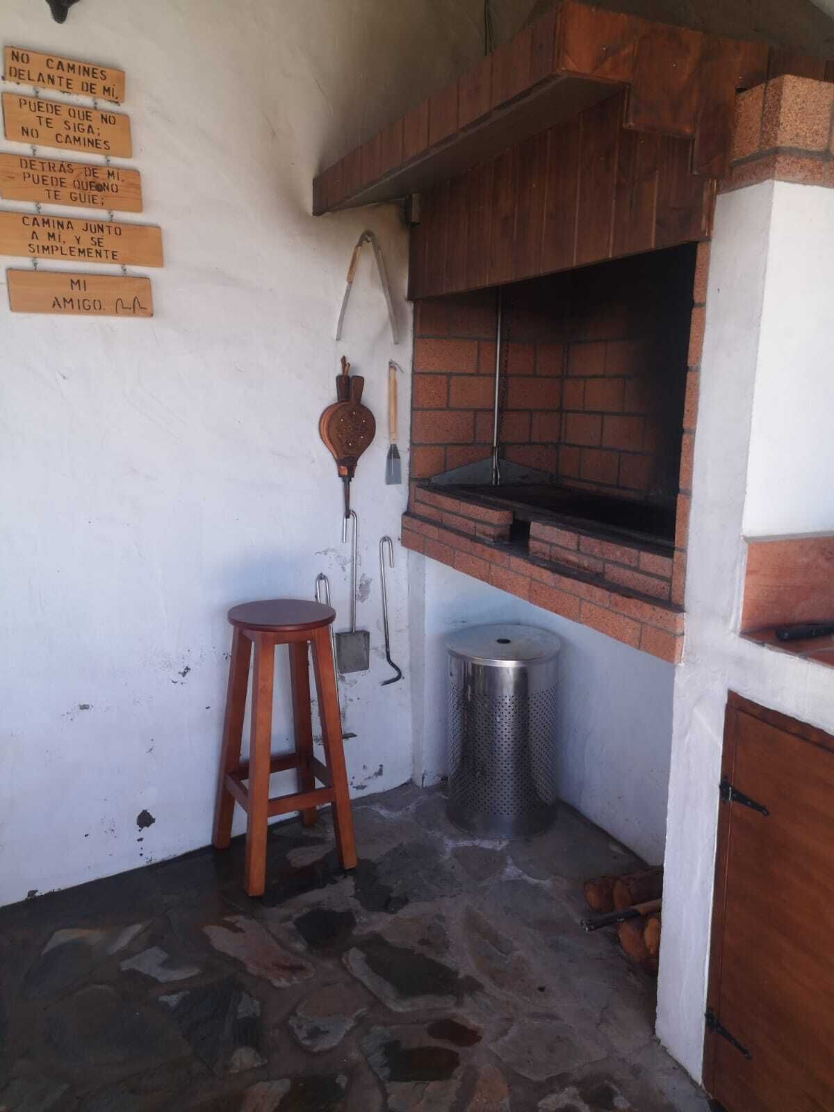 Une petite cuisine avec un four en briques, un tabouret en bois et une poubelle.