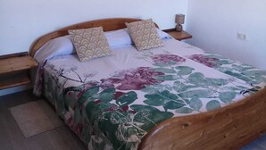 A bedroom with a wooden bed, floral bedding, and two wall-mounted paintings. - VILLA SILA (El Paso)
