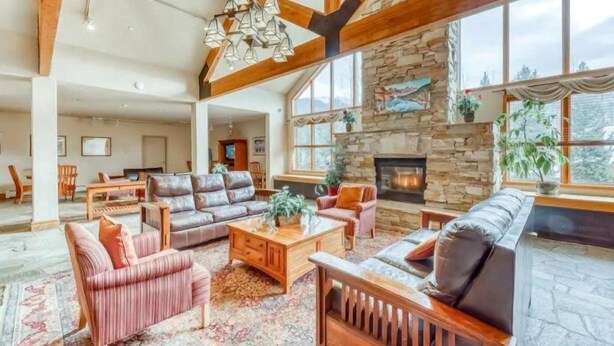 A spacious living room with a stone fireplace, leather sofas, and a large window offering a view of the outdoors. - Studio Condo at Gateway Lodge in Keystone (Keystone)