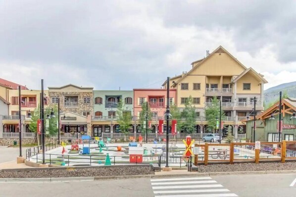 A street view with colorful buildings, a pedestrian crossing, and a fenced area with a picnic table. - Studio Condo at Gateway Lodge in Keystone (Keystone)
