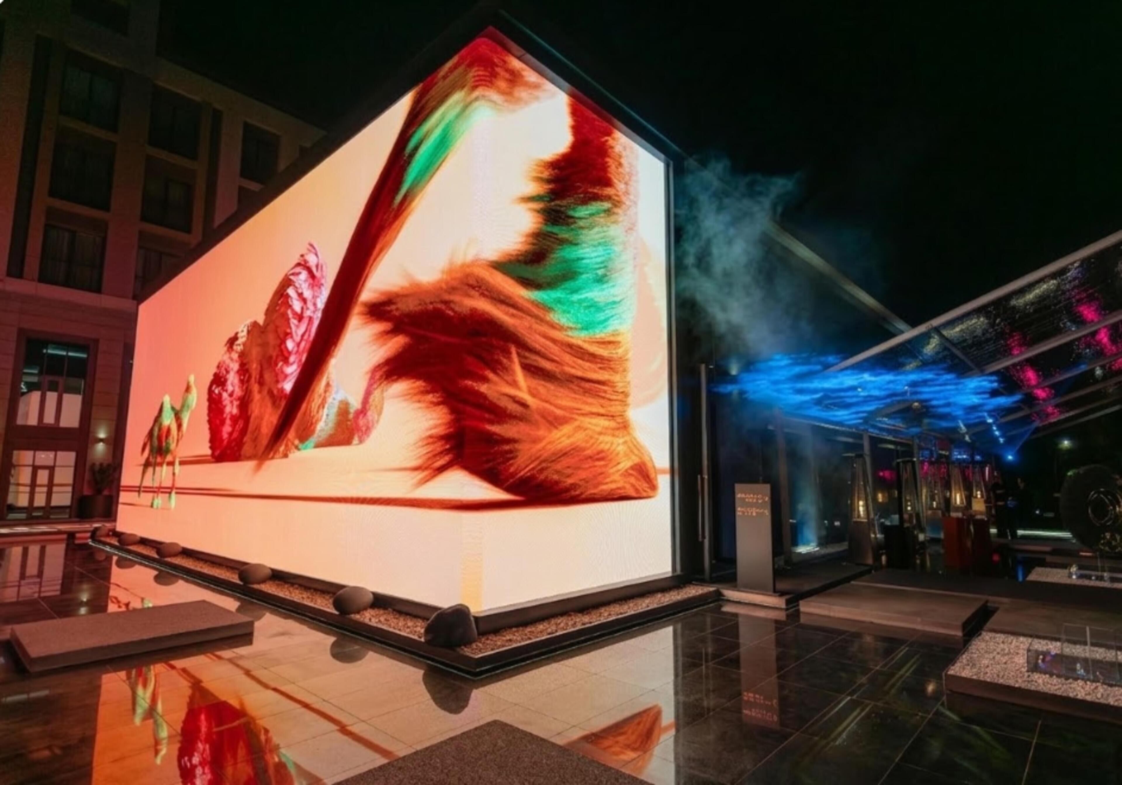Un gran cartel digital con arte abstracto, un suelo reflectante y fachada de un edificio moderno.