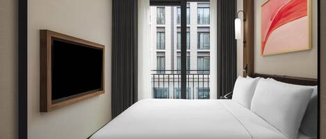 A hotel room with a large bed, a flat-screen TV mounted on the wall, a window with a view of buildings, and a modern abstract painting on the wall.