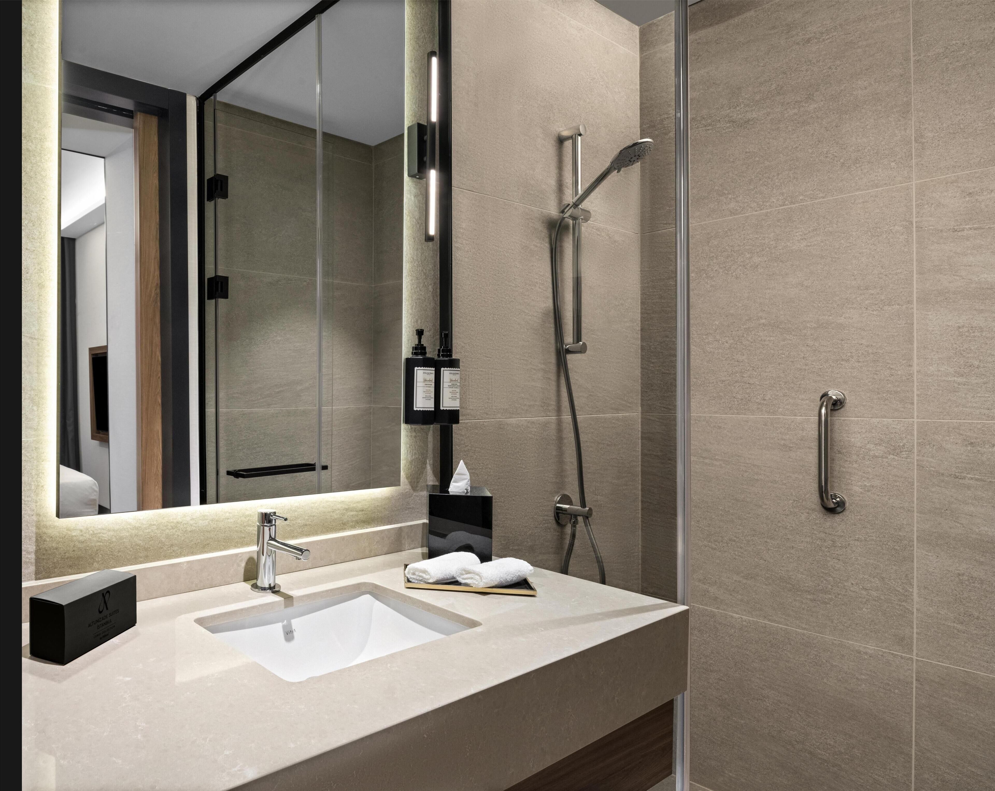 A modern bathroom with a large mirror, a sink, a shower, and a towel rack.