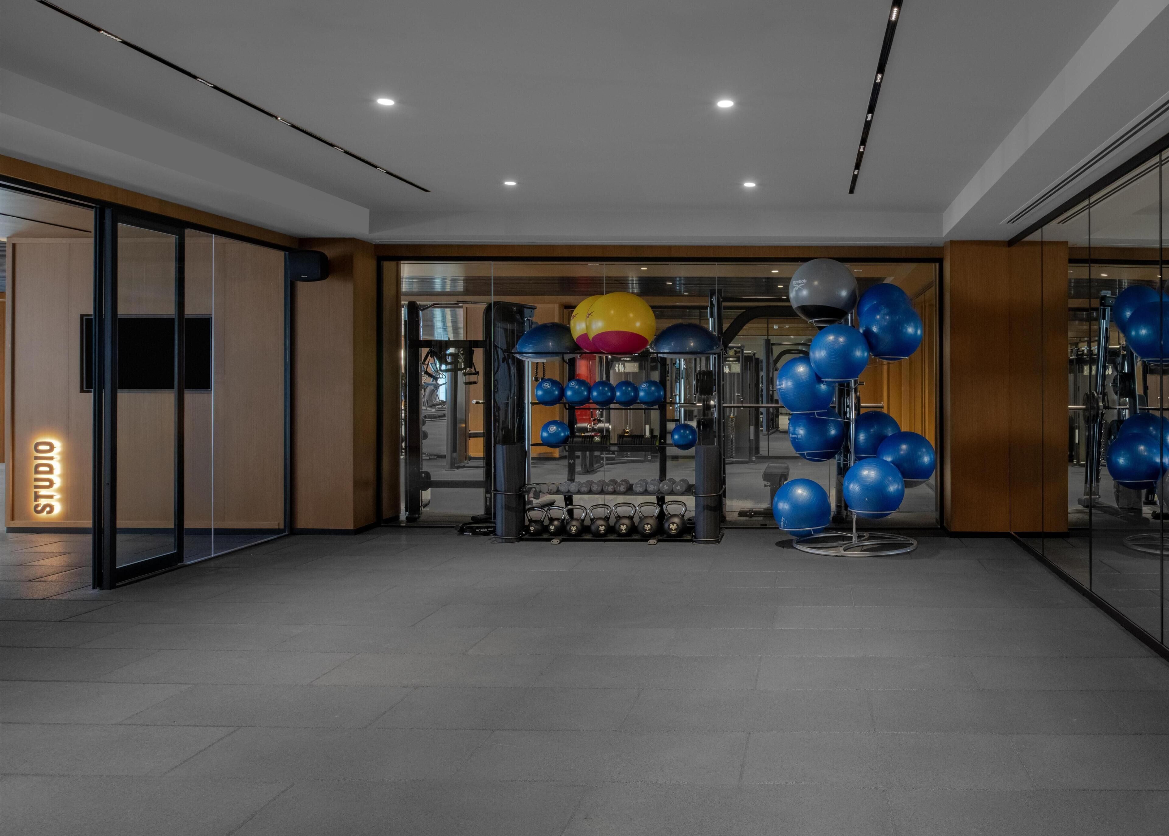 A modern gym with exercise equipment, a mirrored wall, and a 'STUDIO' sign.