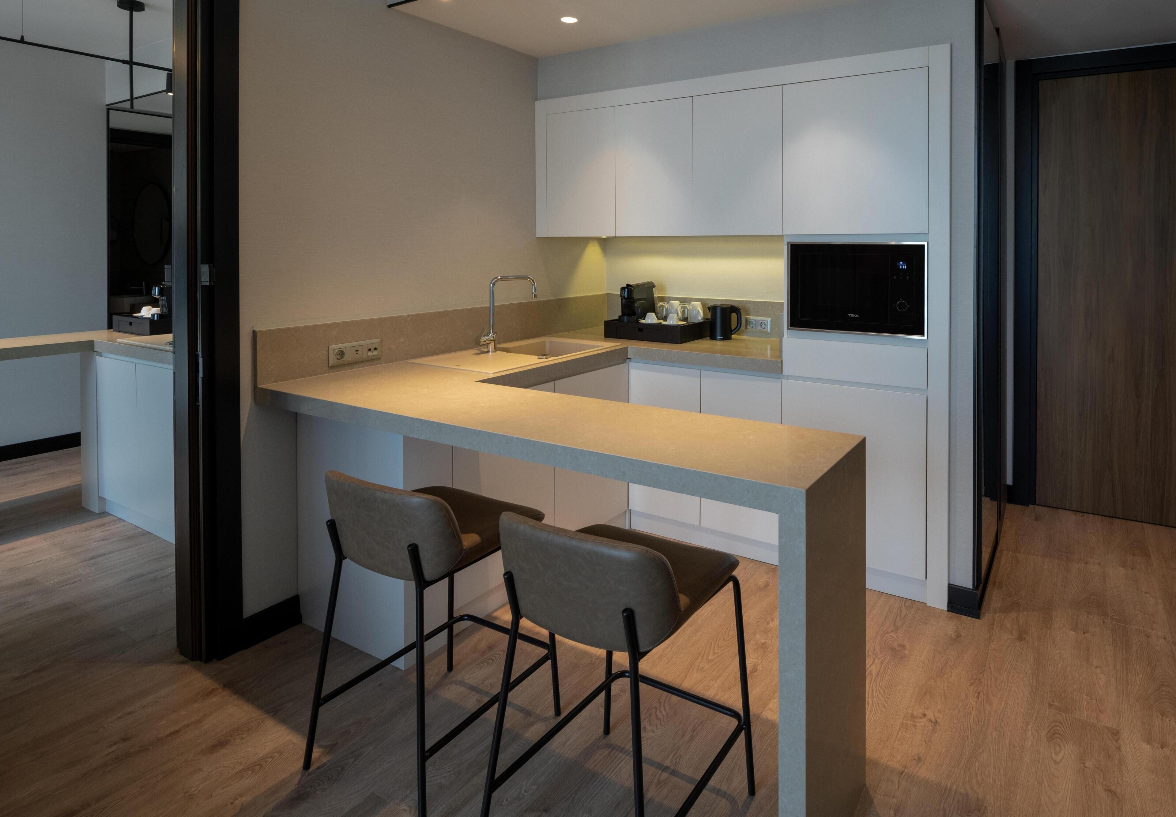 Una cocina moderna con una isla central, dos taburetes de bar, un lavaplatos empotrado y una cafetera.