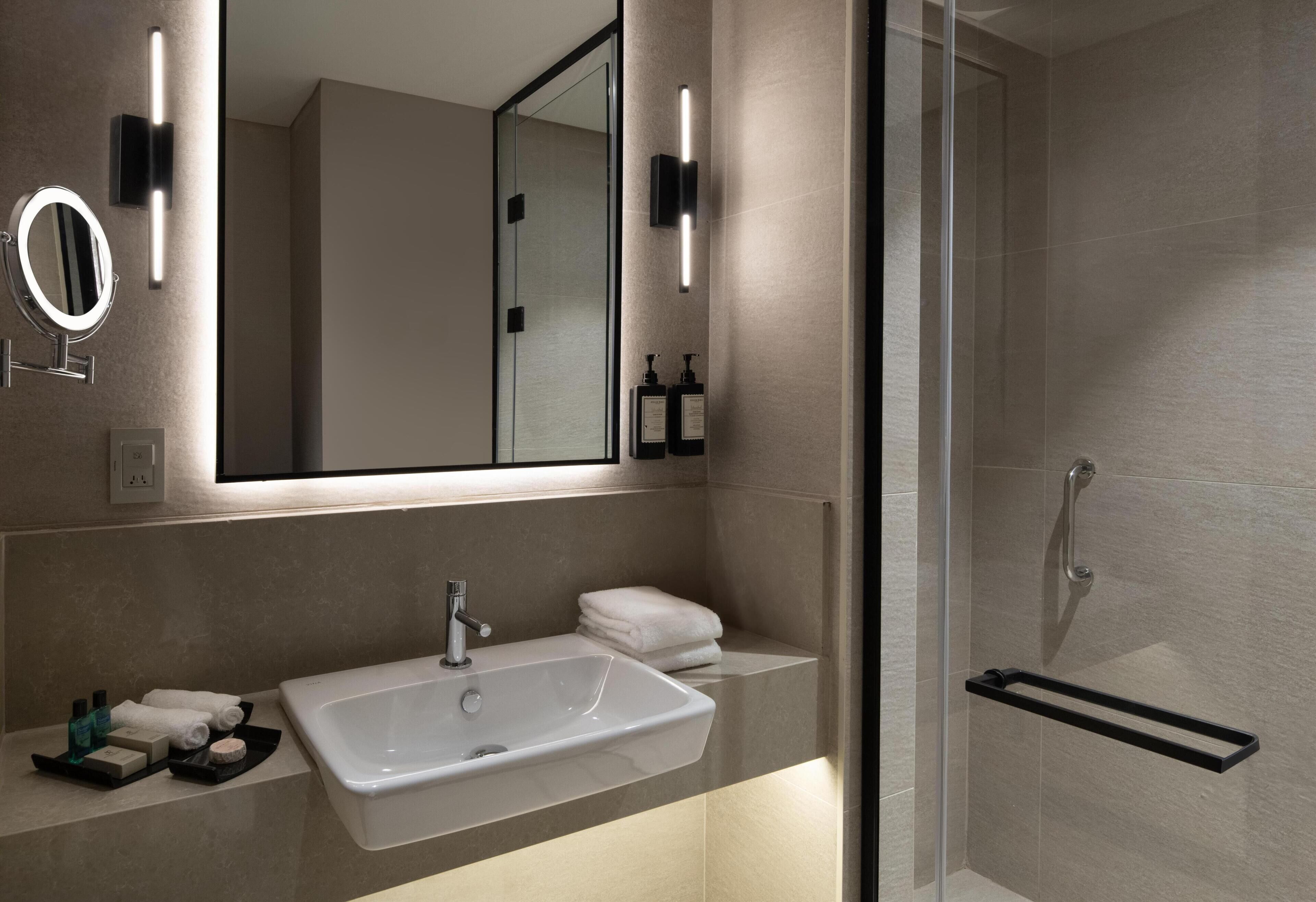 A modern bathroom with a large mirror, a sink, and a glass shower enclosure.