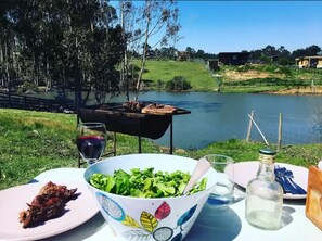 Enjoy a tranquil meal overlooking the serene lake with a grill and beautifully set table.