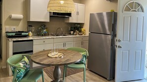 A modern kitchen with a round wooden table, green chairs, a stainless steel refrigerator, and a hanging light fixture. - Palmy Jungalow, a Serene Studio, Mount Dora (Mount Dora)
