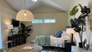 A modern bedroom with a bed, bedside tables, a round wooden table, chairs, and large plants. - Palmy Jungalow, a Serene Studio, Mount Dora (Mount Dora)