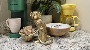 A kitchen counter with a KEURIG coffee maker, a white mug, a golden monkey figurine, a plant, and a yellow coffee pot. - Palmy Jungalow, a Serene Studio, Mount Dora (Mount Dora)