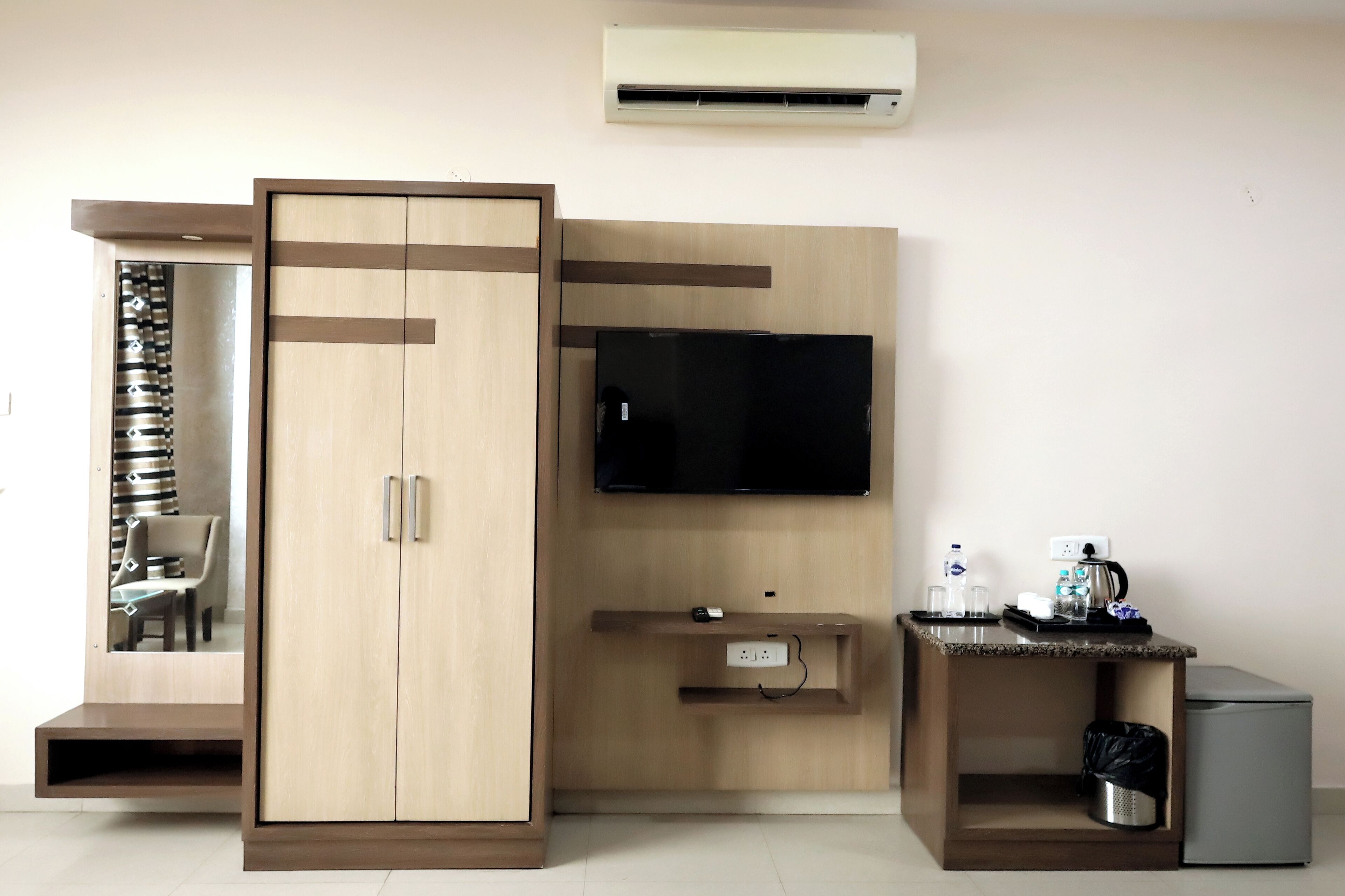 A hotel room with a wardrobe, a television, a small desk with a coffee maker, and a trash bin.