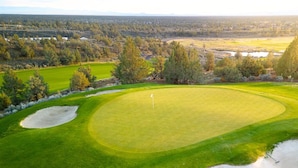 Campo de golf con un mástil de bandera, bunkers de arena y diversos árboles y arbustos.