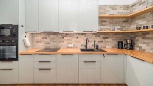 Una cocina moderna con gabinetes grises, un microondas negro, un horno empotrado, un lavamanos negro y una cafetera sobre una encimera de madera.