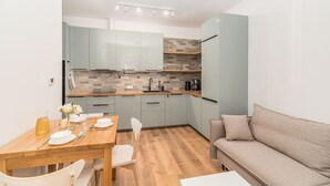 Cocina compacta con armarios azul claro, una mesa de comedor de madera dispuesta con platos y vasos, y un sofá beige en la zona de estar.