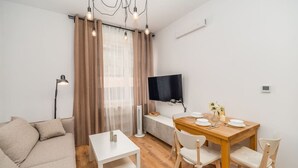 Una sala de estar moderna con un sofá, una mesa de comedor y sillas. Hay un televisor de pantalla plana en la pared y una lámpara de pie.