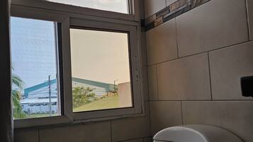A bathroom with a toilet, a window, and a view of a building outside.