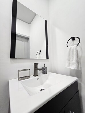 A bathroom with a white sink, a black towel ring, and a mirror. - HK Group Hotel (La Ceiba)