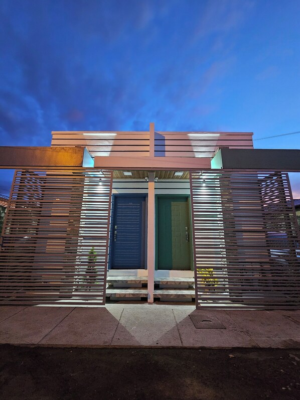 A modern building with a prominent entrance featuring a blue door and a green door, flanked by metal slats. - HK Group Hotel (La Ceiba)