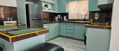 Cocina compacta con armarios color turquesa, encimera negra y suelo de mármol.