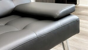 Un canapé moderne en cuir noir, doté d’un socle métallique, est placé dans une pièce dont le sol est recouvert de parquet clair et où l’on aperçoit, à l’arrière-plan, une commode en bois foncé.