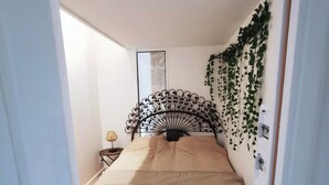 A bedroom with a bed, a bedside table, a lamp, and a decorative wall hanging.