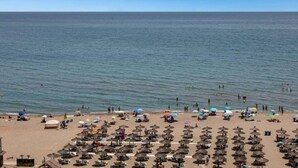 A beach with numerous umbrellas and sun loungers, a clear sky, and calm sea. - Carvajal Beach Apartment. Maravillosas Vistas (Benalmádena)