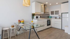 A modern kitchen with white cabinets, a glass dining table, and a hanging light fixture. - Carvajal Beach Apartment. Maravillosas Vistas (Benalmádena)