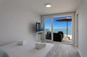 Ein Hotelzimmer mit Bett, Fernseher und einem Balkon mit Meerblick.