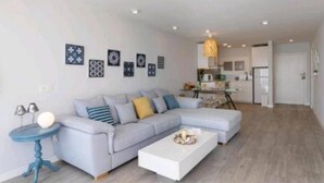 A modern living room with a grey sectional sofa, a white coffee table, and a blue side table. - Carvajal Beach Apartment. Maravillosas Vistas (Benalmádena)