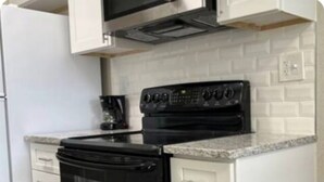 A kitchen with white cabinets, a black stove, and a microwave above the stove. - Modern Lauderhill Condo/ Private Room and Bathroom (Lauderdale Lakes)