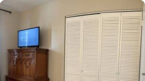 A bedroom with a wooden dresser, a television on top, and a set of white louvered closets. - Modern Lauderhill Condo/ Private Room and Bathroom (Lauderdale Lakes)