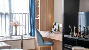 A modern hotel room with a wooden desk, a chair, a small table with a plant, and a TV stand with figurines. - Guangzhou Hantao International Apartment (Guangzhou)